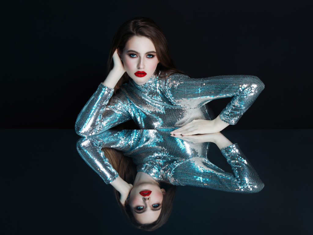 Woman in futuristic sequin top and her mirror reflection